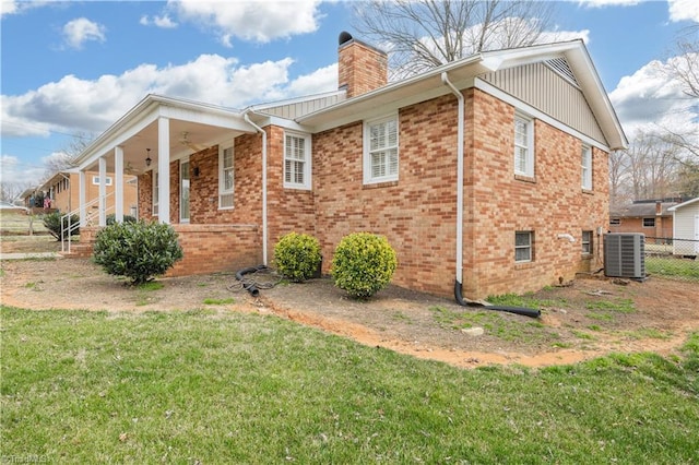 view of side of property featuring central AC, fence, a yard, brick siding, and a chimney