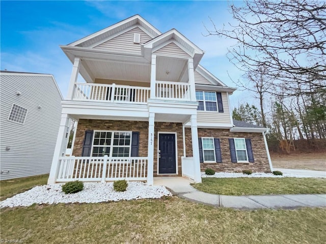 view of front of house with a balcony, covered porch, stone siding, and a front yard