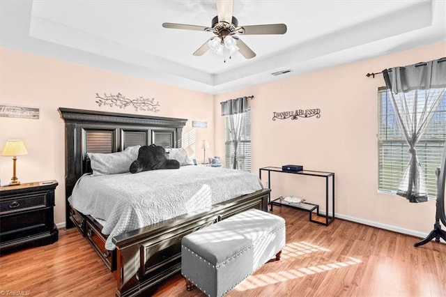 bedroom featuring ceiling fan, light hardwood / wood-style floors, and a tray ceiling