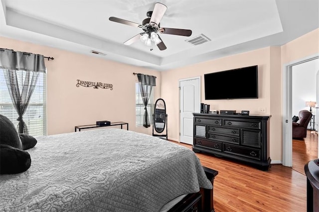 bedroom featuring a tray ceiling, multiple windows, ceiling fan, and wood-type flooring