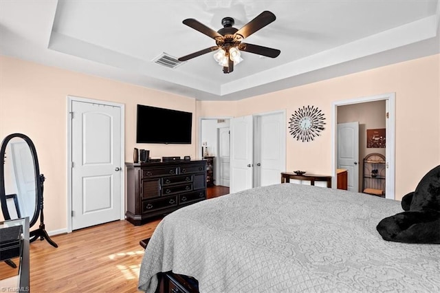 bedroom featuring light wood-type flooring, a tray ceiling, and ceiling fan