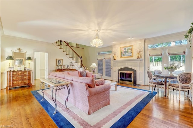 living room with stairway, a fireplace, ornamental molding, a notable chandelier, and light wood-type flooring