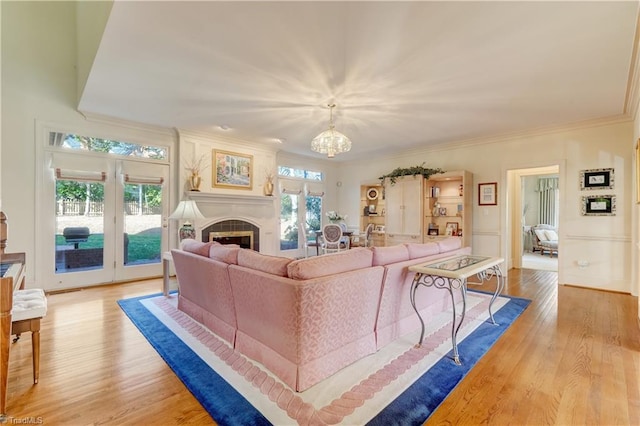 living room with light wood-style flooring, a fireplace, an inviting chandelier, and ornamental molding