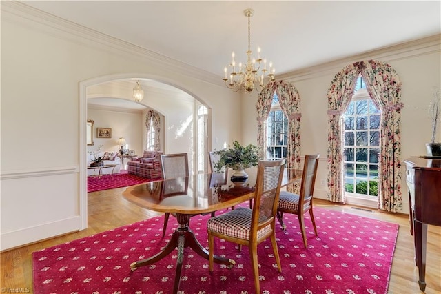 dining room with an inviting chandelier, crown molding, wood finished floors, and arched walkways