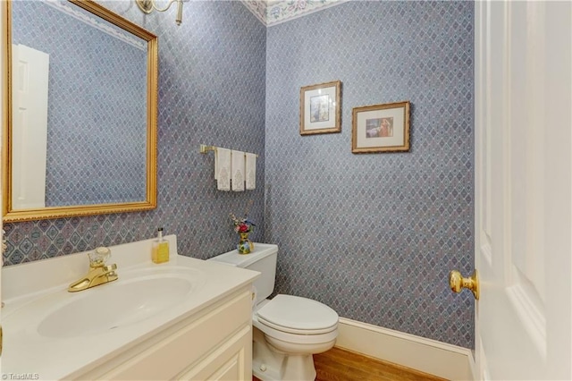 bathroom with wallpapered walls, wood finished floors, toilet, and vanity