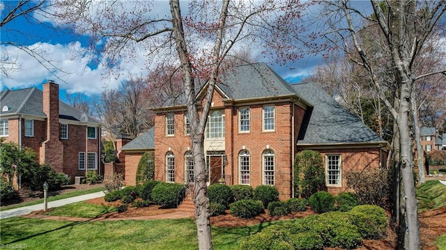 colonial inspired home with brick siding, a front lawn, and roof with shingles