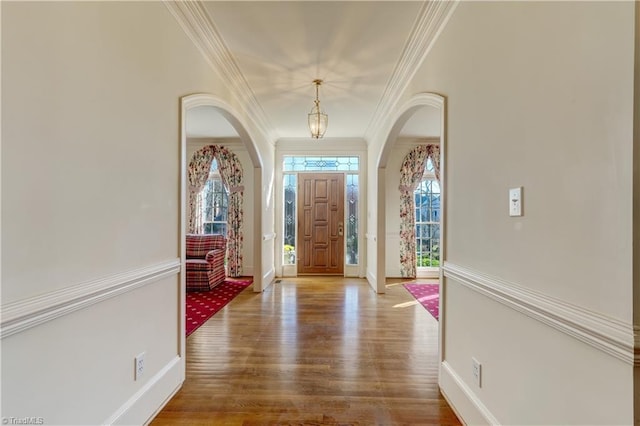 foyer entrance featuring arched walkways, ornamental molding, baseboards, and wood finished floors