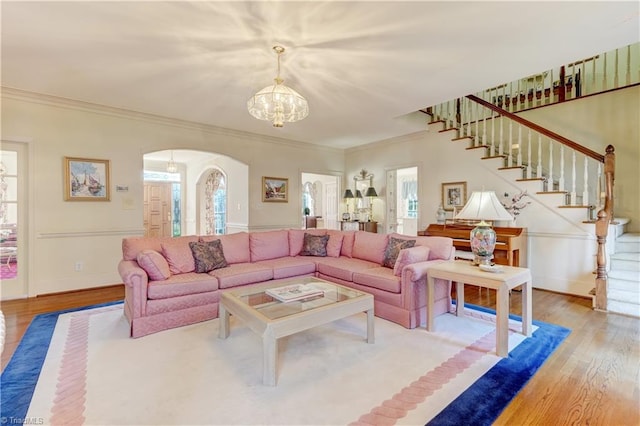 living area with stairway, wood finished floors, arched walkways, ornamental molding, and a chandelier