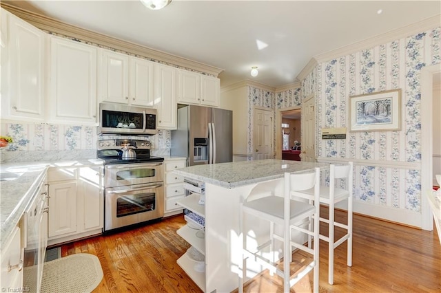 kitchen with a breakfast bar area, wallpapered walls, light wood-style flooring, ornamental molding, and stainless steel appliances