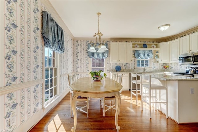 dining room featuring a notable chandelier, wallpapered walls, crown molding, and wood finished floors