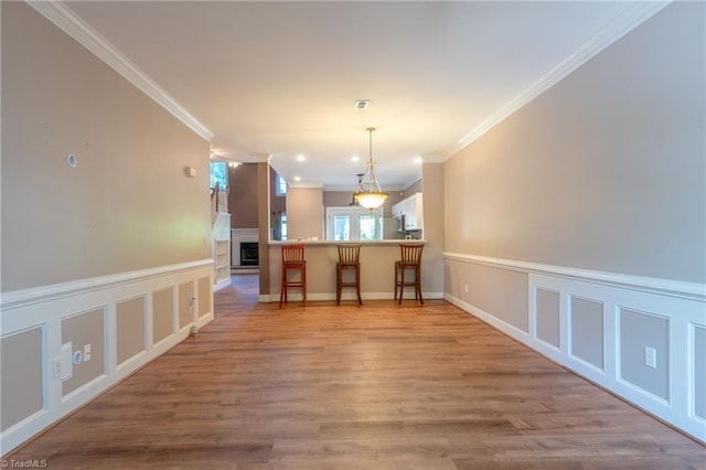 interior space with light hardwood / wood-style floors, kitchen peninsula, a kitchen bar, decorative light fixtures, and crown molding