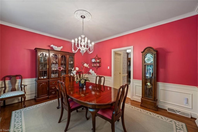dining area featuring a chandelier, visible vents, dark wood-type flooring, and a wainscoted wall