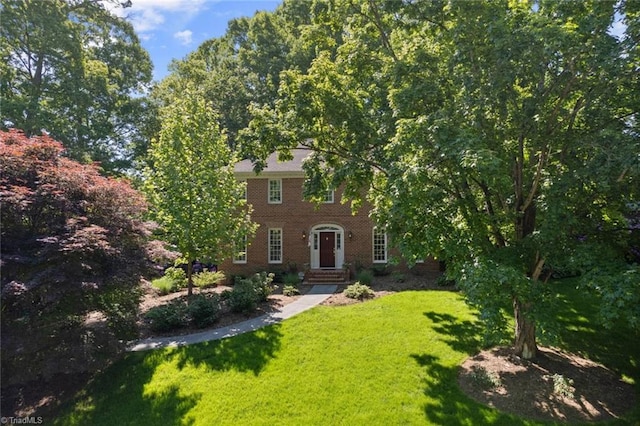 colonial inspired home featuring brick siding and a front yard