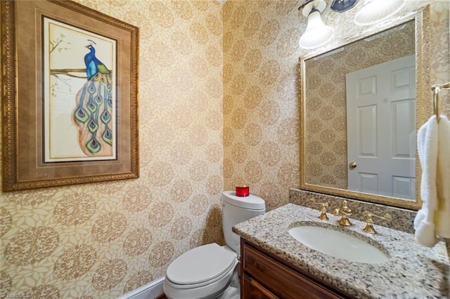 bathroom with toilet, wallpapered walls, and vanity