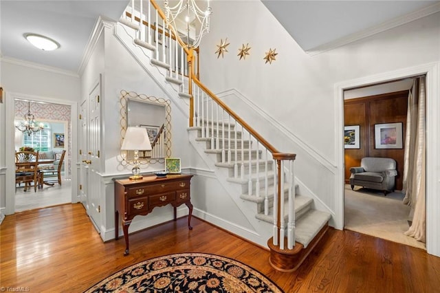 staircase featuring baseboards, a notable chandelier, ornamental molding, and wood finished floors