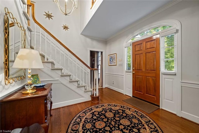 foyer entrance featuring wainscoting, wood finished floors, stairway, a chandelier, and ornamental molding