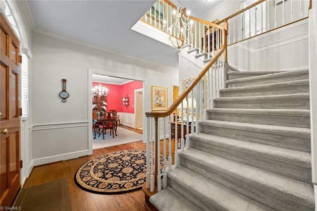 entrance foyer featuring ornamental molding, wood finished floors, stairway, a wainscoted wall, and a chandelier