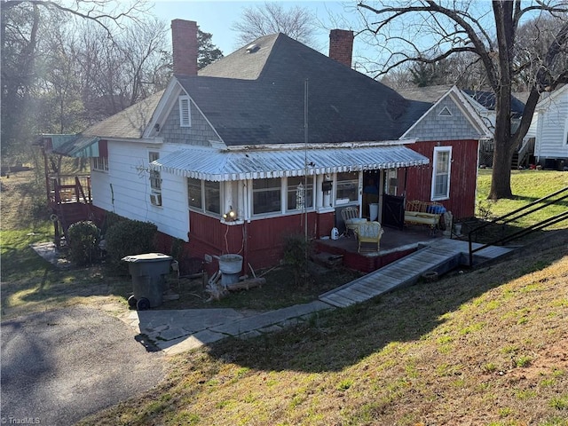 view of front of house featuring a front yard, roof with shingles, and a chimney