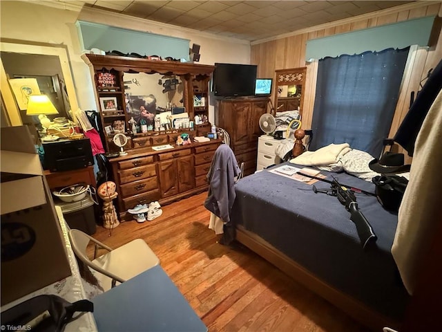 bedroom with crown molding, light wood-style flooring, and wood walls