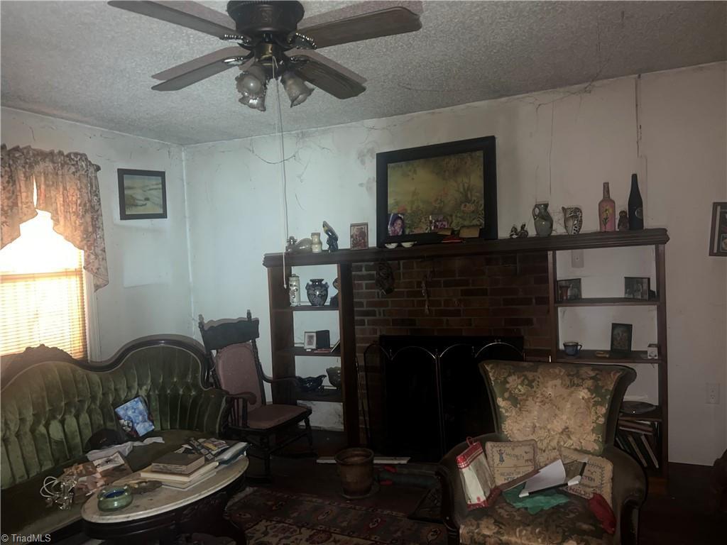 sitting room featuring ceiling fan, a brick fireplace, and a textured ceiling