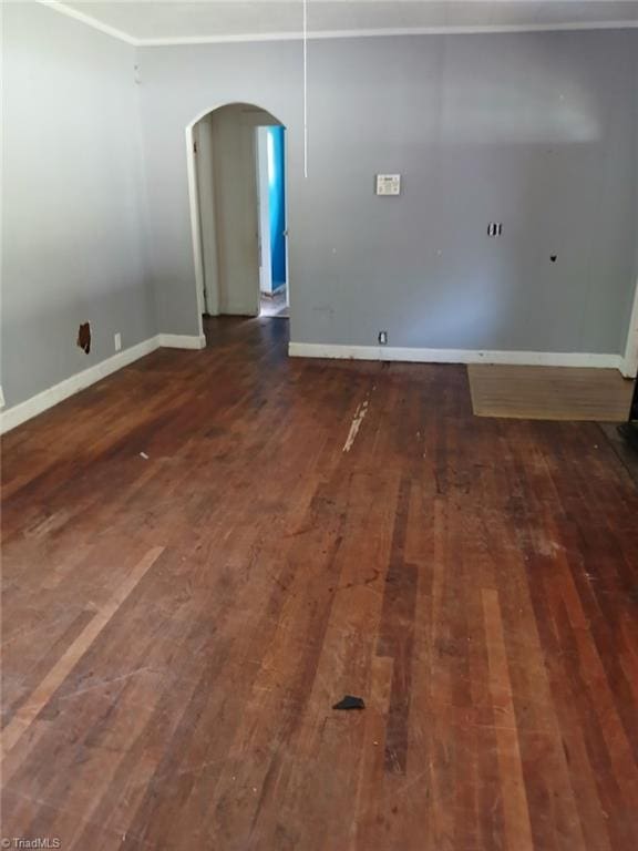 unfurnished room featuring arched walkways, ornamental molding, hardwood / wood-style flooring, and baseboards