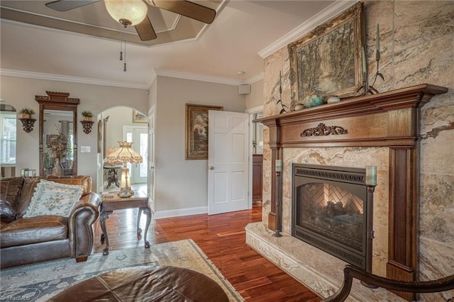 living room featuring a high end fireplace, dark wood-type flooring, ornamental molding, and ceiling fan