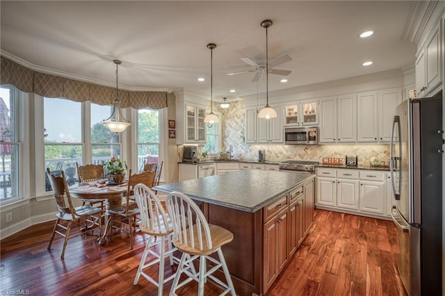 kitchen featuring stainless steel appliances, a kitchen island, white cabinets, and decorative light fixtures