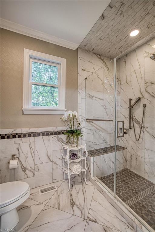 bathroom featuring ornamental molding, toilet, an enclosed shower, and tile walls