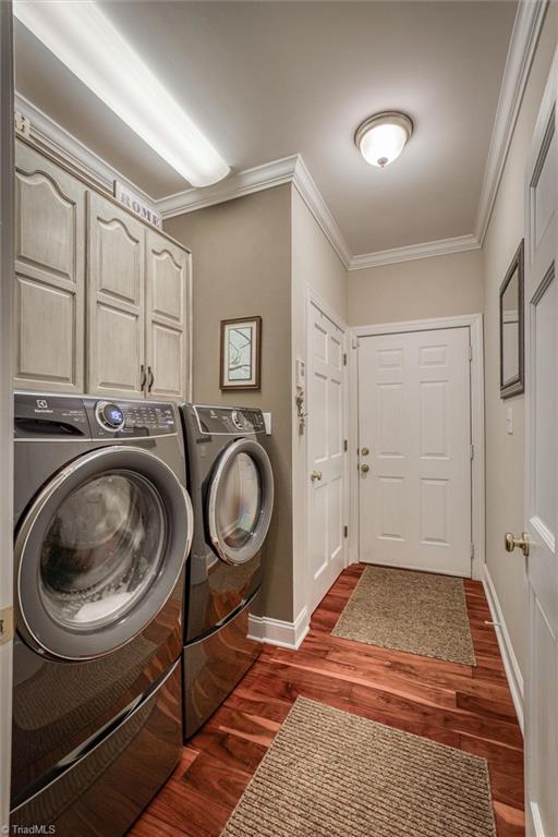 clothes washing area with dark wood-type flooring, ornamental molding, washing machine and dryer, and cabinets