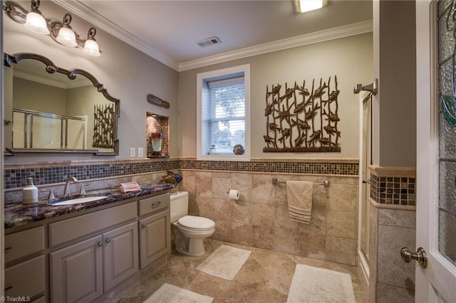 bathroom featuring tile walls, vanity, ornamental molding, toilet, and a shower with door