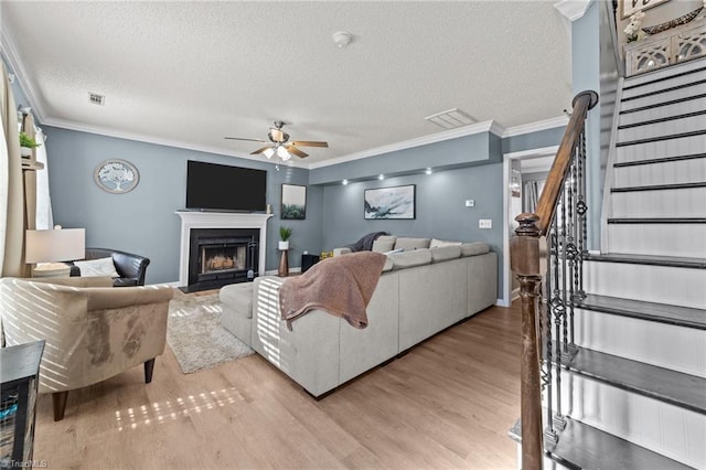 living room featuring ceiling fan, ornamental molding, light hardwood / wood-style flooring, and a textured ceiling