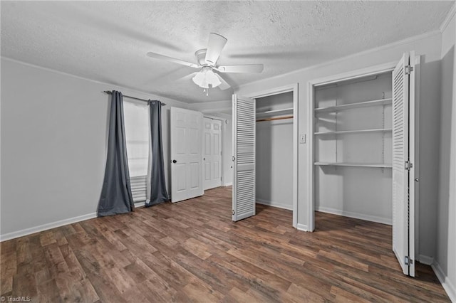 unfurnished bedroom featuring a textured ceiling, ornamental molding, dark hardwood / wood-style flooring, two closets, and ceiling fan