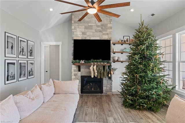 living room featuring a stone fireplace, ceiling fan, wood-type flooring, and vaulted ceiling