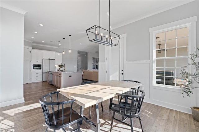 dining room with a chandelier, crown molding, sink, and light hardwood / wood-style floors