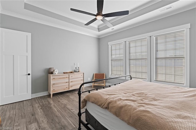 bedroom with a raised ceiling, ceiling fan, crown molding, and wood-type flooring