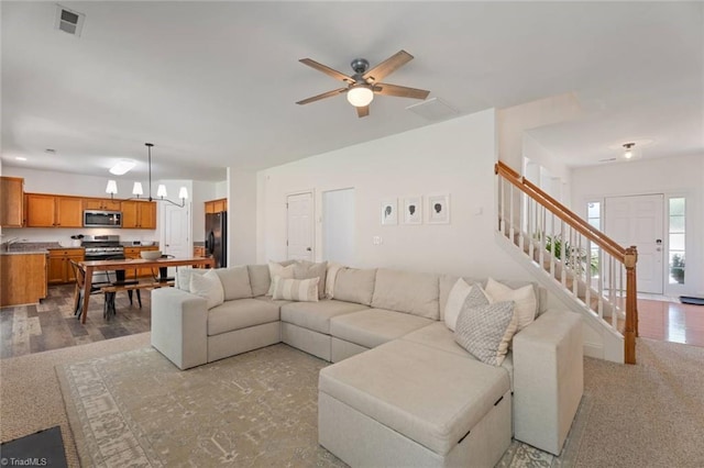 living room featuring visible vents, stairs, and ceiling fan with notable chandelier