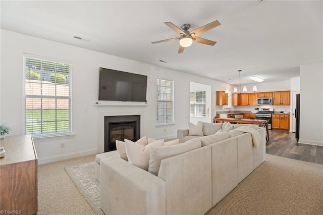 living area featuring visible vents, a glass covered fireplace, ceiling fan, and baseboards