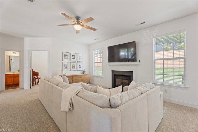 living area featuring visible vents, a glass covered fireplace, baseboards, light colored carpet, and a ceiling fan
