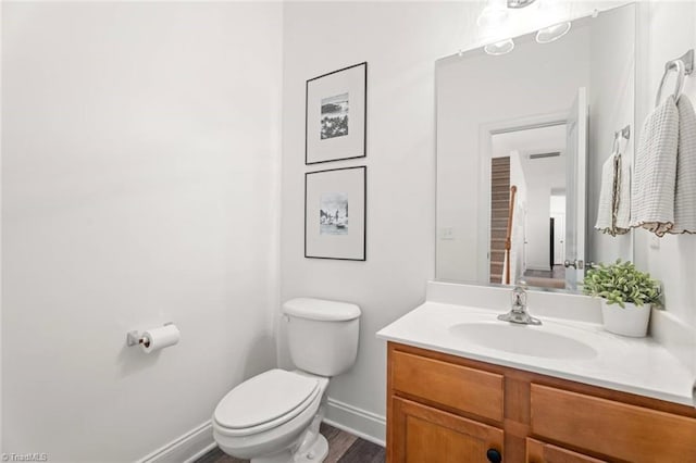 half bathroom featuring visible vents, wood finished floors, vanity, baseboards, and toilet