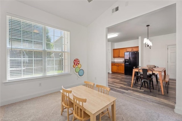 carpeted dining room featuring an inviting chandelier, baseboards, lofted ceiling, and visible vents