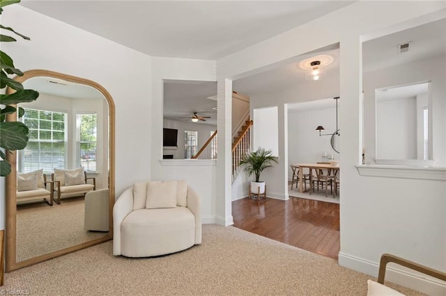living area with visible vents, baseboards, ceiling fan, stairway, and carpet flooring