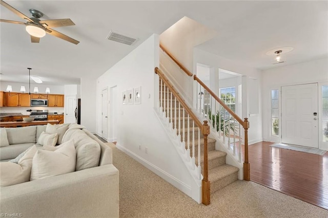 interior space featuring ceiling fan, visible vents, stairway, baseboards, and light wood-style floors