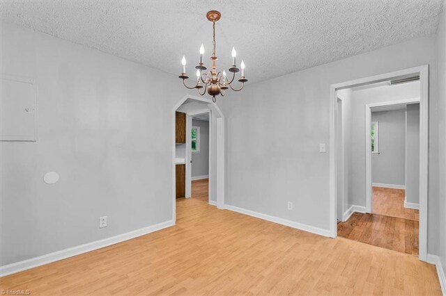 1655 Oakleigh Rd, Mcleansville, NC 27301 - unfurnished room with arched walkways, light wood-style flooring, a chandelier, and a textured ceiling