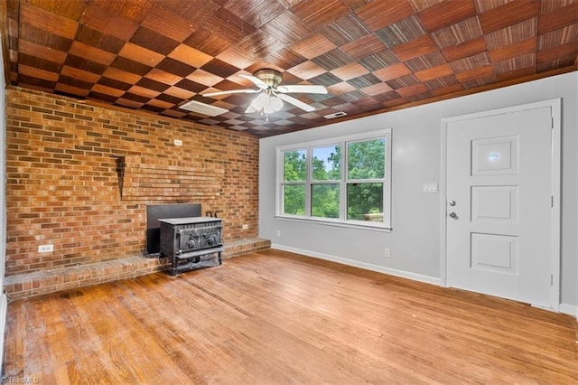 1655 Oakleigh Rd, Mcleansville, NC 27301 - unfurnished living room with a ceiling fan, a wood stove, wood finished floors, and brick wall