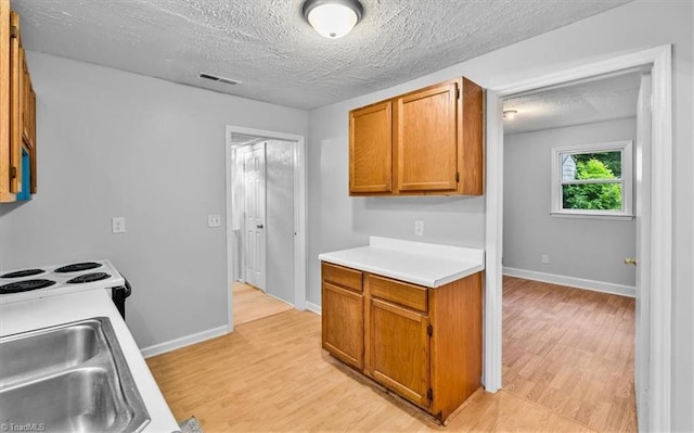 1655 Oakleigh Rd, Mcleansville, NC 27301 - kitchen featuring light wood finished floors, light countertops, a textured ceiling, brown cabinets, and electric range
