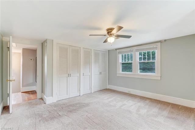 unfurnished bedroom with two closets, light colored carpet, and ceiling fan