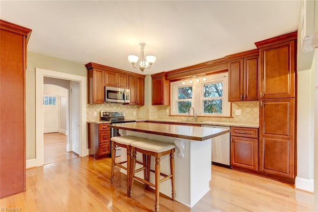 kitchen featuring pendant lighting, a kitchen island, appliances with stainless steel finishes, tasteful backsplash, and light hardwood / wood-style floors