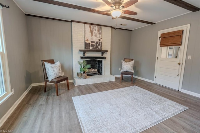 unfurnished room featuring beamed ceiling, ceiling fan, hardwood / wood-style floors, and a fireplace