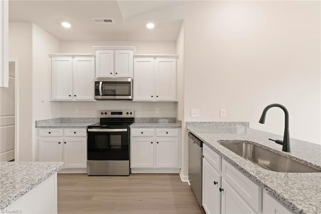 kitchen with light stone countertops, white cabinetry, sink, stainless steel appliances, and light hardwood / wood-style flooring