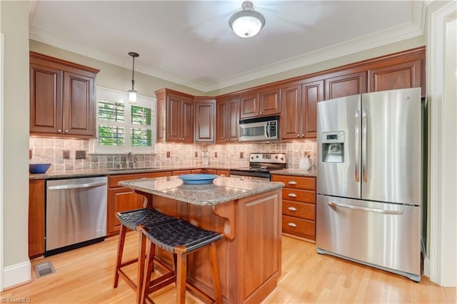 kitchen with stone countertops, a center island, stainless steel appliances, decorative light fixtures, and light hardwood / wood-style flooring